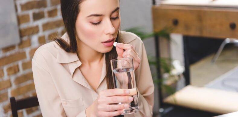 young sick businesswoman taking medicine at workplace